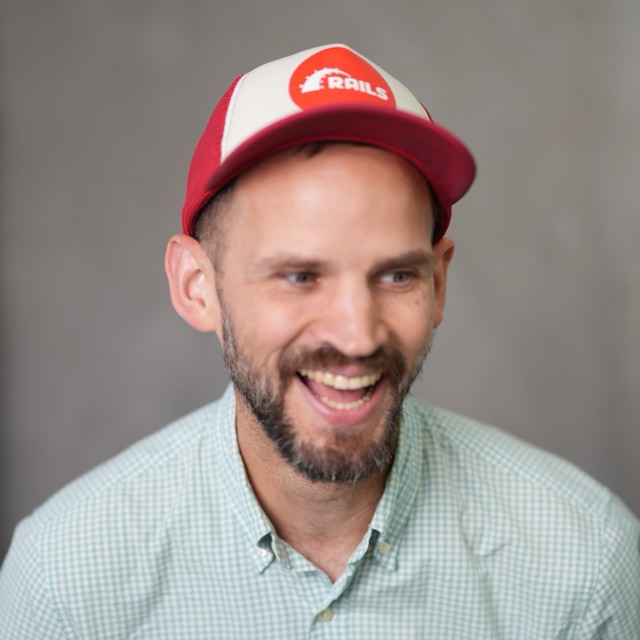 Christopher Moeller, laughing, in a red Ruby on Rails trucker hat